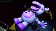 a purple and white stuffed animal is laying on a table in a dark room with its mouth open .