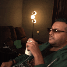 a man wearing sunglasses sits in a chair holding a can of soda