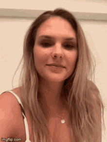 a woman with long blonde hair is wearing a white tank top and necklace .