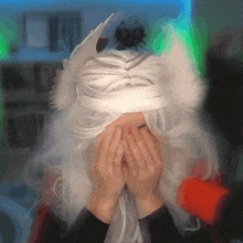 a person wearing a white wig with ears covering their face with their hands