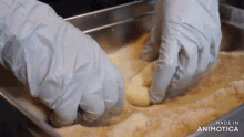 a person wearing gloves is dipping a piece of food in a pan .