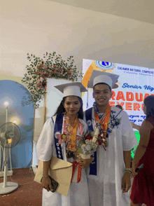two graduates pose for a photo in front of a sign that says calamba national comprehension