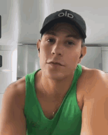 a man wearing a green tank top and a black hat with the word old on it