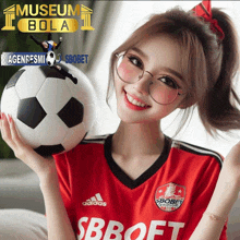 a girl in a red adidas jersey holds a soccer ball in her hands
