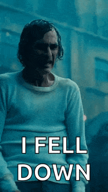 a man in a white sweater is standing in front of a building and says i fell down .
