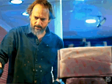 a man with a beard is standing in front of a box with the letter h in the corner