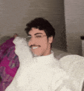 a man wearing glasses and a white shirt is sitting on a couch and smiling .