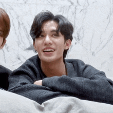 a young man wearing a black sweater and earrings smiles