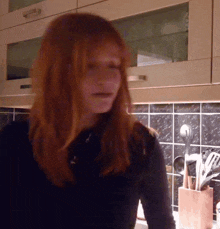 a woman with red hair is standing in a kitchen with utensils on the counter
