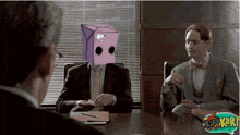 a man with a purple box on his head sits at a table with other men