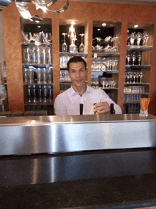 a man in a white shirt stands behind a bar holding a glass