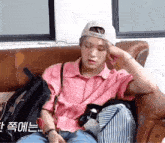 a young man in a pink shirt and baseball cap is sitting on a couch .