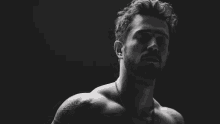 a black and white photo of a shirtless man with tattoos on his arms