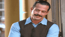 a man with a mustache wearing a vest and blue shirt