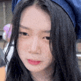 a woman with long black hair wearing a blue hat looks at the camera
