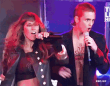 a woman singing into a microphone next to a man with a tattoo