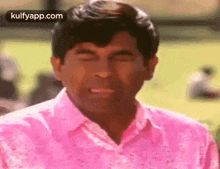 the man is wearing a pink shirt and making a funny face .