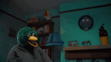 a green stuffed animal with a yellow beak and big eyes is holding a yellow object .