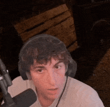 a man wearing headphones is sitting in front of a microphone and looking at the camera .