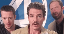 a man with a mustache is standing next to two other men in front of a blue and white logo .