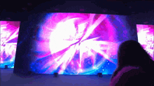 a woman stands in front of a large screen that shows a purple and blue light