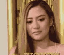 a woman with long hair and hoop earrings is standing in front of a door and looking at the camera .