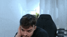 a man with a beard is sitting in a gaming chair and covering his ears .