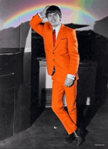 a man in an orange suit and red tie is standing in front of a rainbow