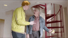 two men are standing in front of a spiral staircase talking to each other .