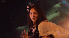 a woman with a flower in her hair stands in front of a screen that says live