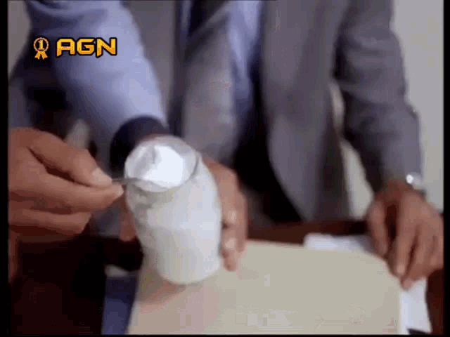 a man in a suit is pouring something into a cup with agn written on it