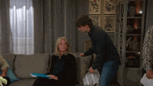 a woman sits on a couch while a man stands behind her