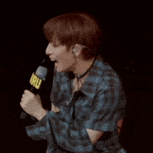 a man in a plaid shirt is holding a microphone and a sign that says haru