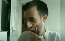 a man in a white shirt is making a funny face while sitting in front of a door .