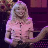a woman in a pink crop top is smiling and holding another woman 's hand on a stage .