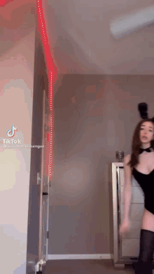 a woman in a bunny costume is dancing in a room with a red light on the wall .