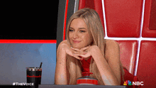 a woman sitting in a chair with a cup of coffee and a nbc logo on the bottom