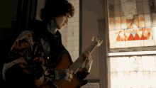 a man playing a guitar in front of a window