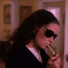a woman wearing sunglasses lighting a cigarette with a lighter