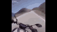 a motorcycle is driving down a road with mountains in the background .