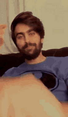 a man with a beard is sitting on a couch and making a face .