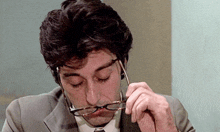a man in a suit and tie is adjusting his glasses while sitting at a table .