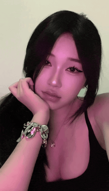 a woman wearing a black tank top and a silver bracelet has her hand on her chin