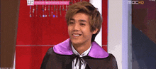 a young man wearing a purple cape smiles in front of a mbc hd sign