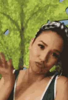 a woman in a green tank top is making a funny face with a tree in the background .