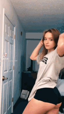 a woman in a t-shirt and shorts is standing in a room .