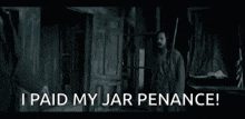 a man with a beard is standing in a dark room with the words `` i paid my jar penance '' .