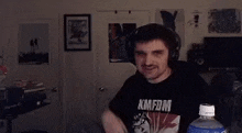 a man wearing headphones and a black shirt with the word boom on it is standing in a dark room .