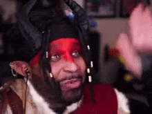a man with red paint on his face and dreadlocks is wearing a black hat and a red scarf .