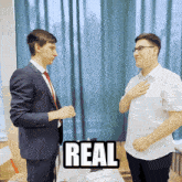two men standing next to each other with a sign that says real on it